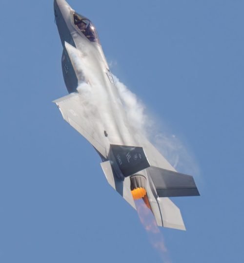 Military fighter jet ascending vertically with engine flames against clear blue sky